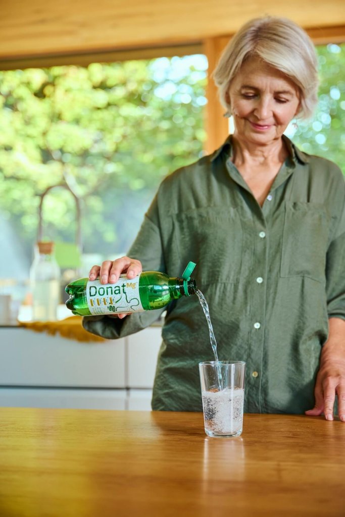 Eine Frau, die natürliches Mineralwasser Donat Mg in ein Glas gießt, das dafür bekannt ist, die Verdauung auf natürliche Weise zu regulieren.